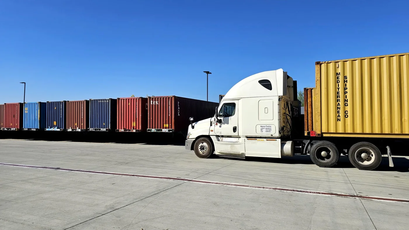 Truck hauling a yellow container through the sunlit Tactical yard