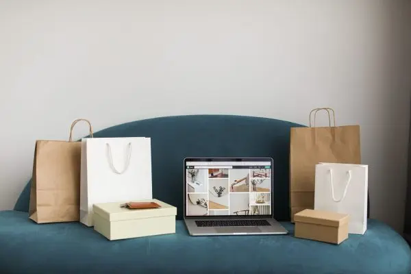 Shopping bags and gift boxes on a teal sofa around a laptop showing an online store