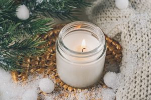 Lit white candle in a glass jar on a woven mat with pine branches and a knit throw